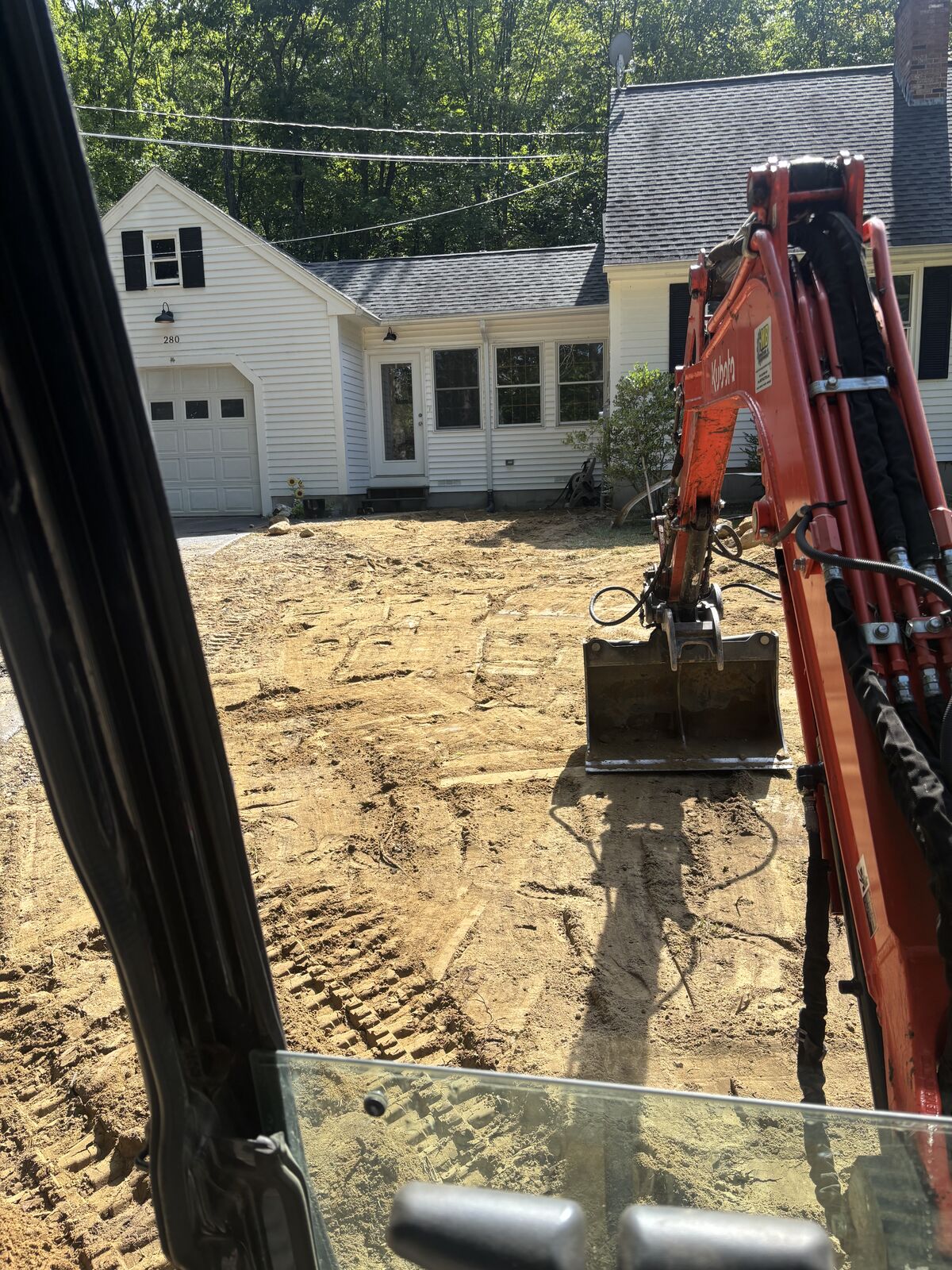 Mini excavator digging the underground service trench beside a house