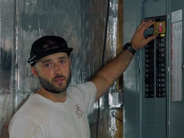 Austin Provencher pointing to the generator interlock on a breaker panel, from his portable generator hookup video