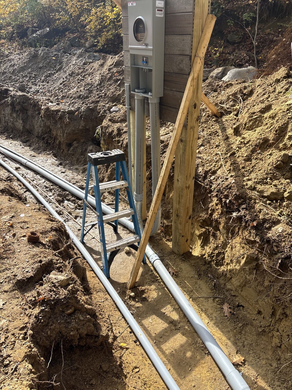 Meter pedestal with conduit stub-ups beside the open trench, a stepladder alongside