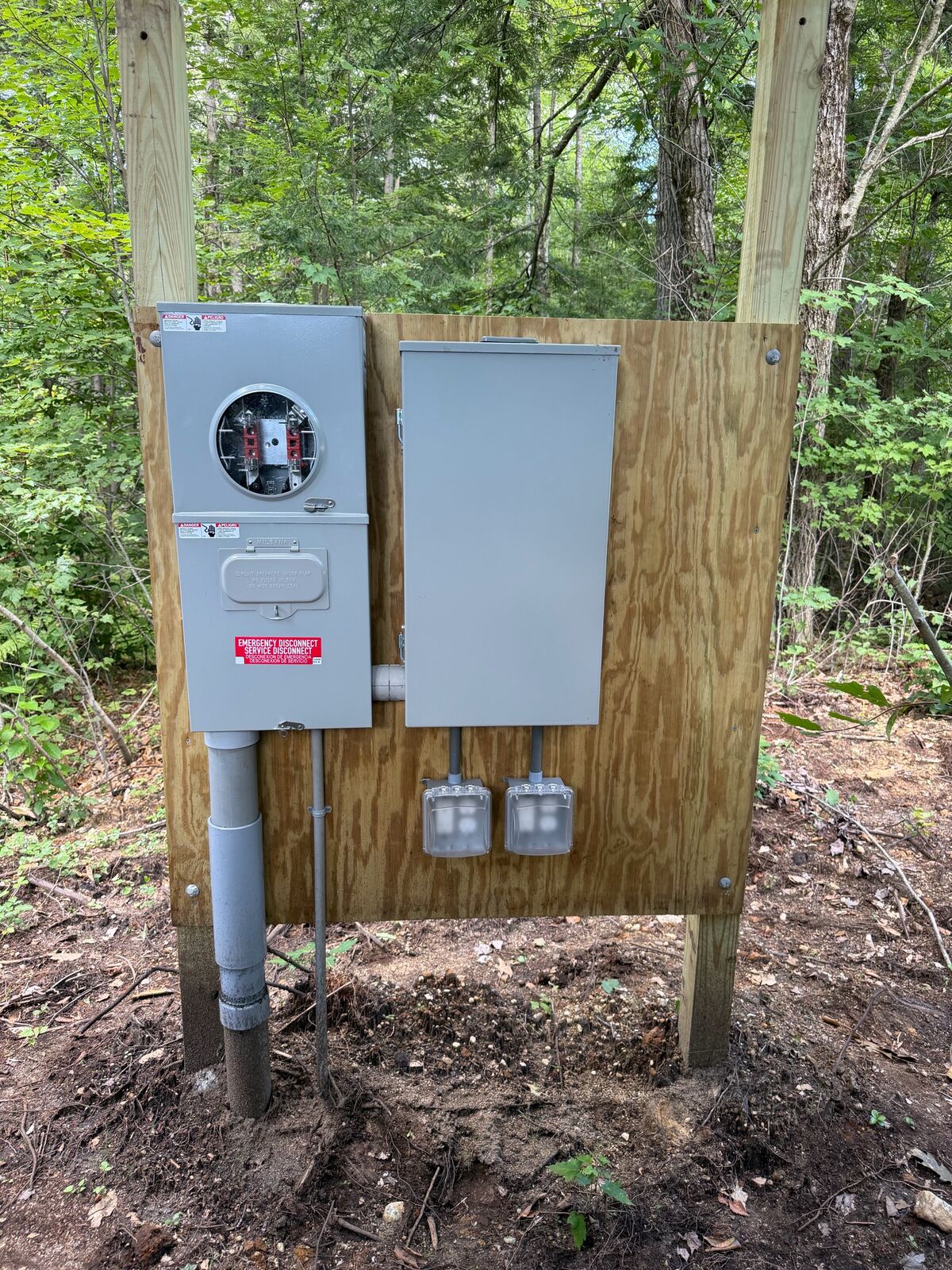 Meter socket, service disconnect and two weatherproof outlets mounted on a wood post pedestal in the woods