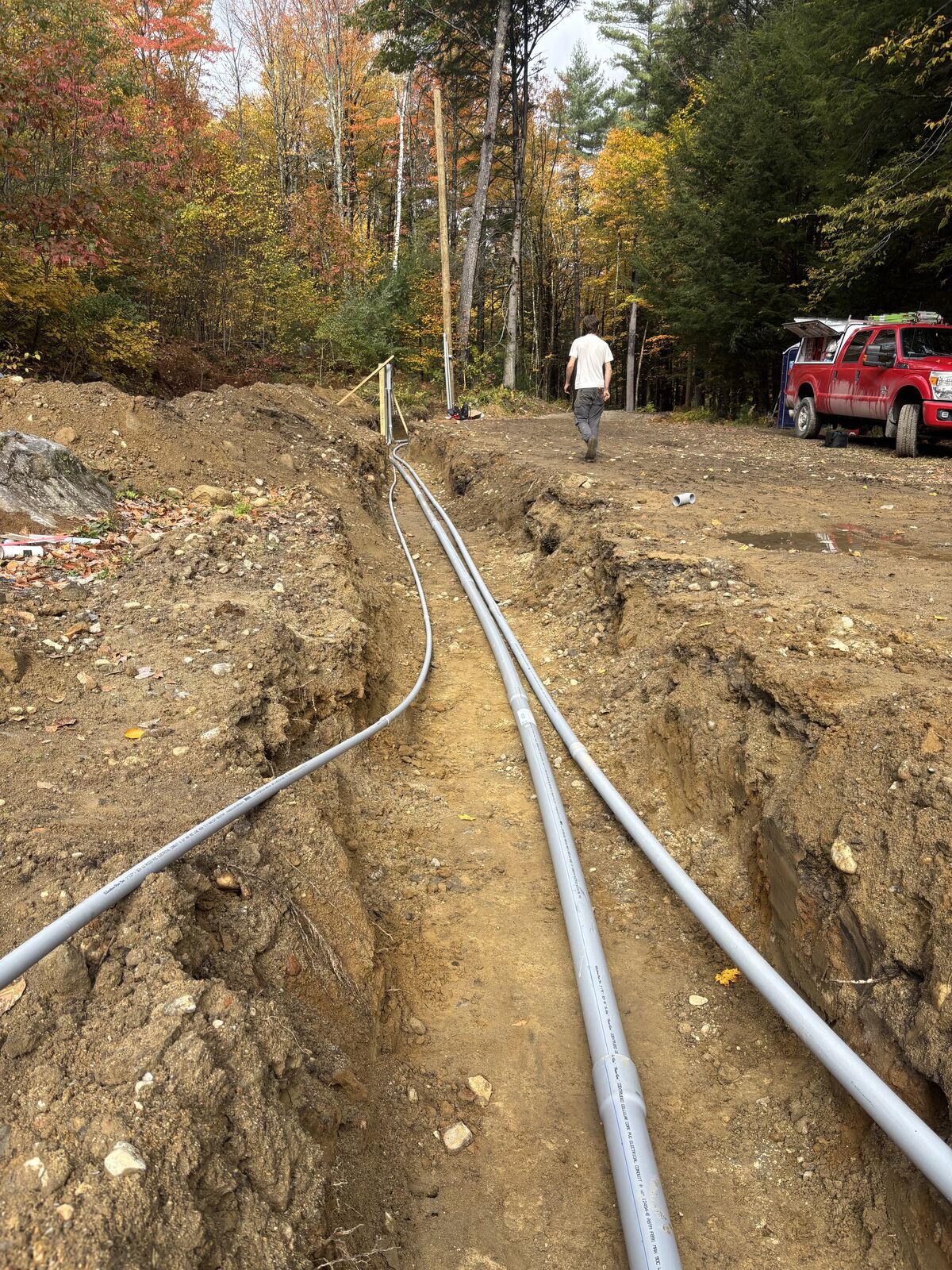 Two runs of gray PVC conduit laid along a long open trench toward the work truck