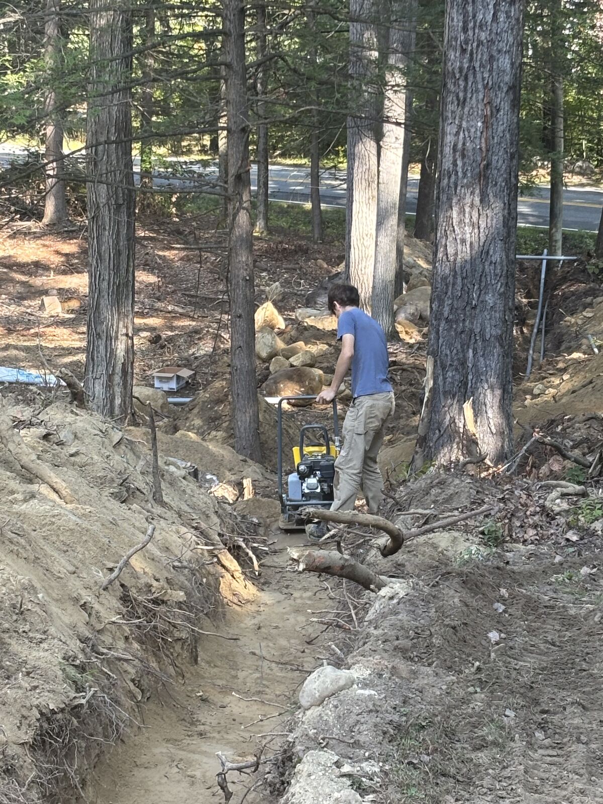 Crew member compacting backfill over the conduit in the service trench