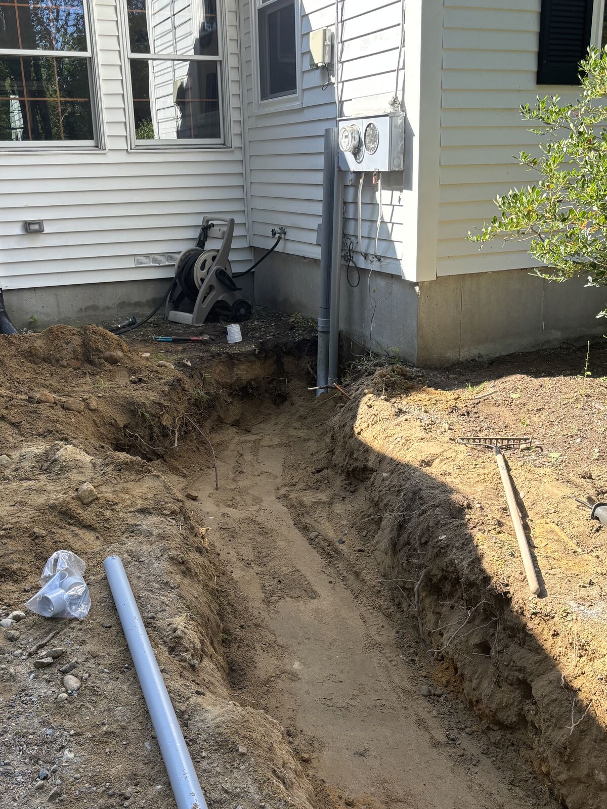 Service trench running up to the side of a white clapboard house, conduit ready to lay